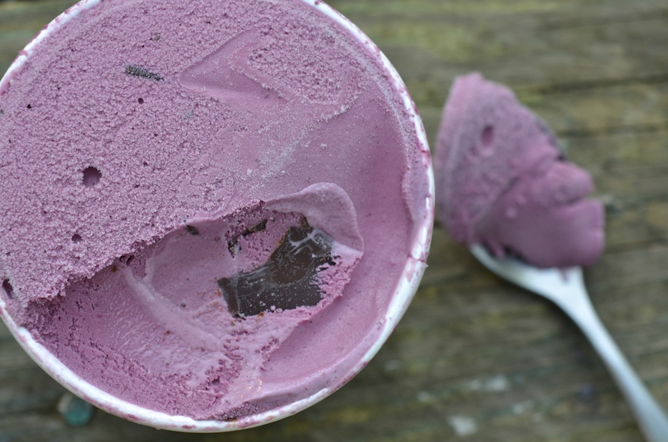 carton of black raspberry ice cream with chocolate chunks and spoon on wooden tabletop