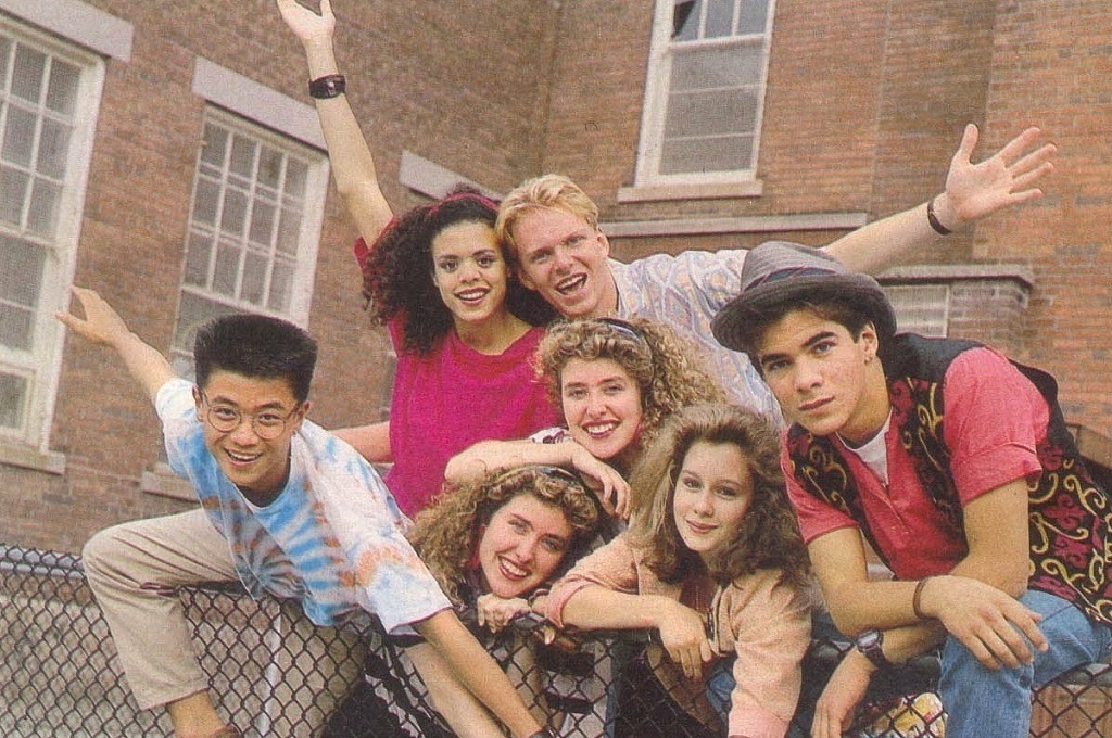 A group of preteens leaning on a fence with their arms out in front of a school building
