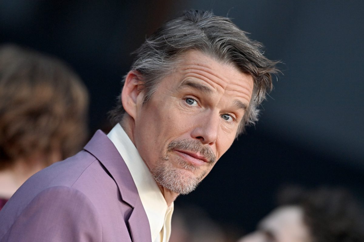 'The Black Phone'-Schauspieler Ethan Hawke trägt eine lila Anzugjacke mit einem leichten Lächeln, das zur Seite schaut