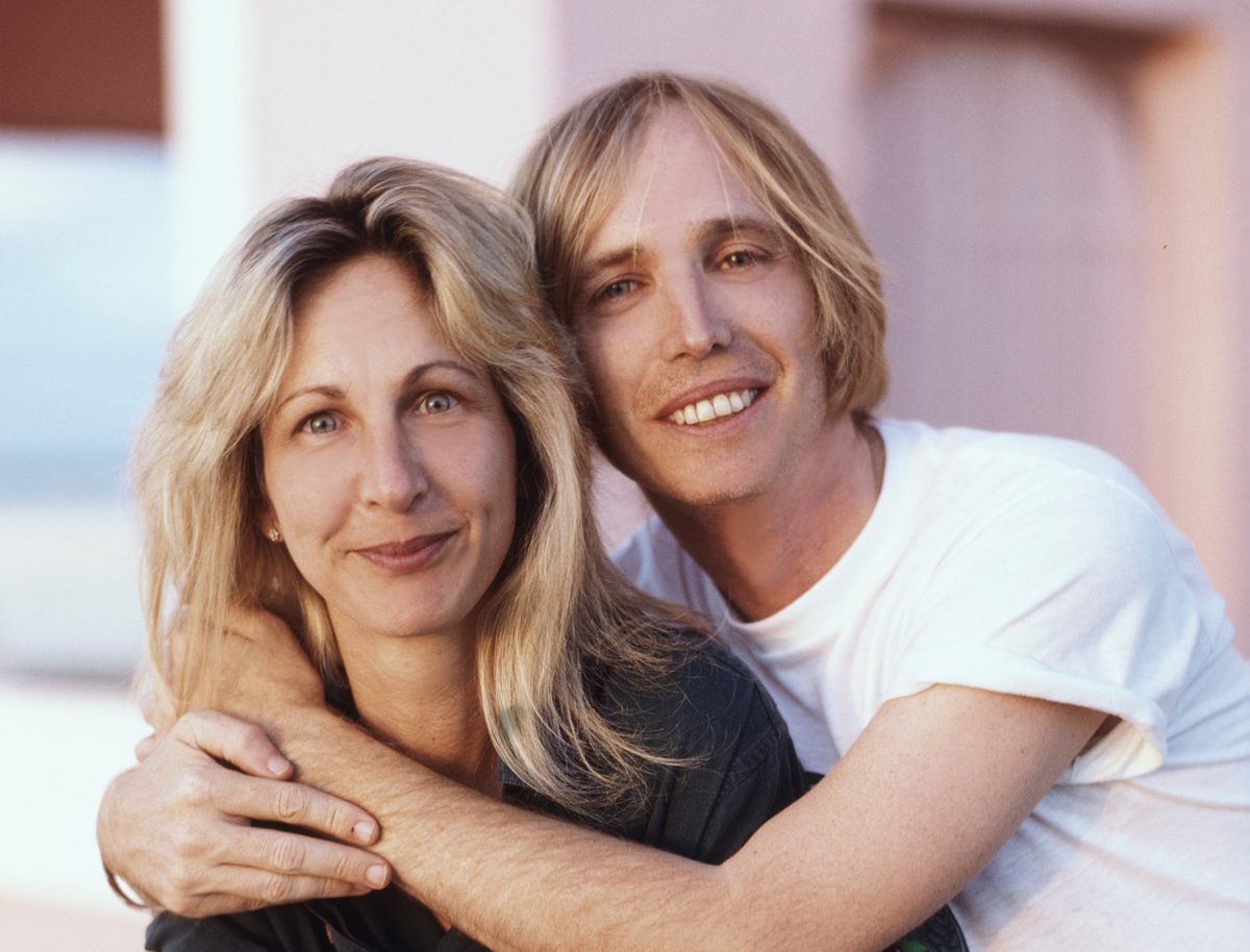 Tom Petty trägt ein weißes Hemd und schlingt seine Arme um Jane Benyo, die ein schwarzes Hemd trägt.