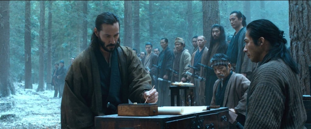 Keanu Reeveswrites something in front of a group of men in the woods in 47 Ronin