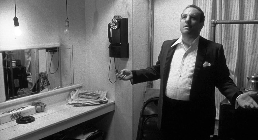 Robert De Niro in makeup prosthetics, wearing a suit with his arms out