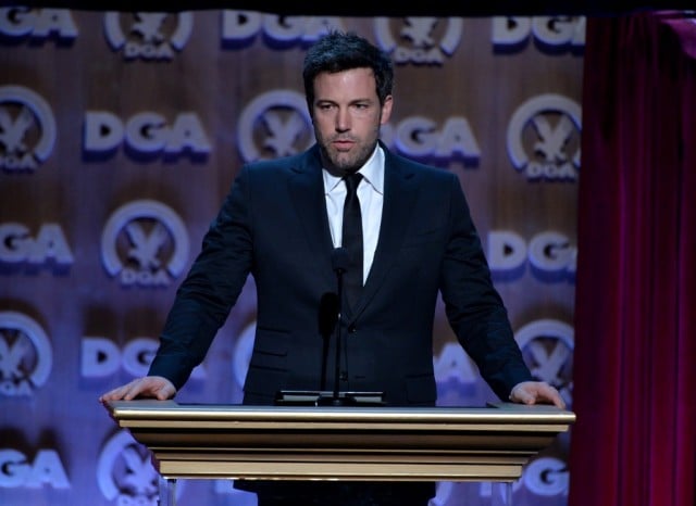 Ben Affleck stands at a podium in a black suit. Ben Affleck stands at a podium in a black suit.