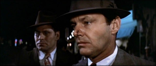 Two men stand next to each other while wearing ties and fedoras in a scene from Chinatown