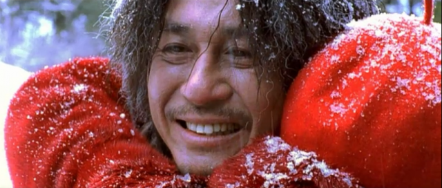 Choi Min-sik smiles while standing in the snow with a big red scarf around his neck in Oldboy
