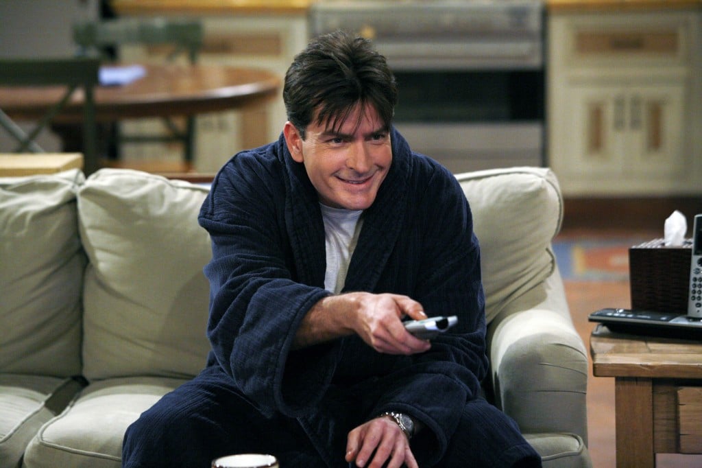Charlie Sheen as Charlie Harper in a bathrobe holding a remote on a couch on Two and a Half Men 