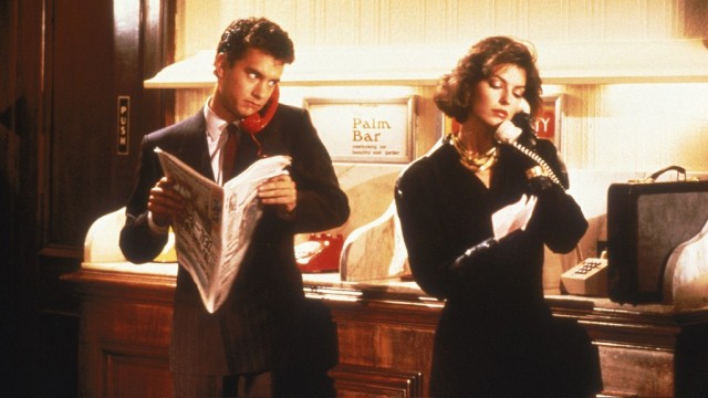 Tom Hanks holds a newspaper while talking on the phone next to a woman in Nothing in Common