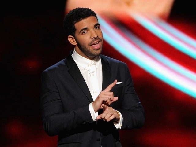 Drake is talking on stage in a black suit.