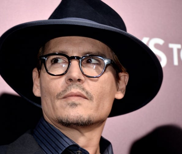 Johnny Depp looking upwards while wearing glasses and a black hat.