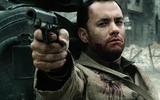 Tom Hanks holds up a gun while wearing a bloodied uniform in Saving Private Ryan