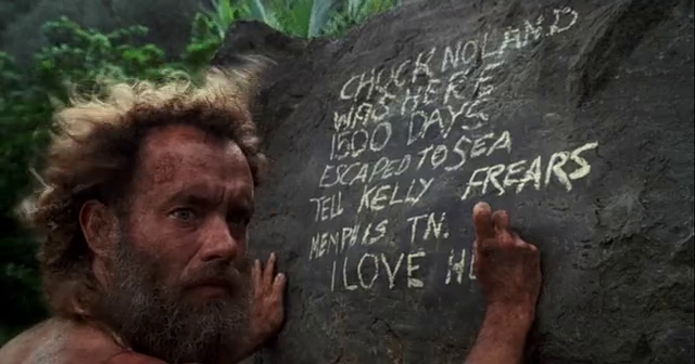 A bearded Tom Hanks carves a message into a rock while stranded on an island in Cast Away