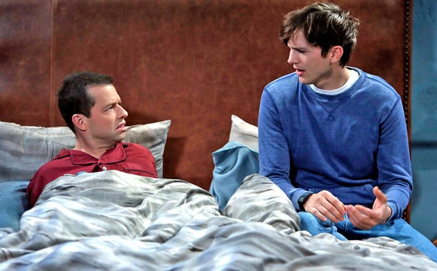 Ashton Kutcher sits next to Jon Cryer in bed in a scene from Two and a Half Men