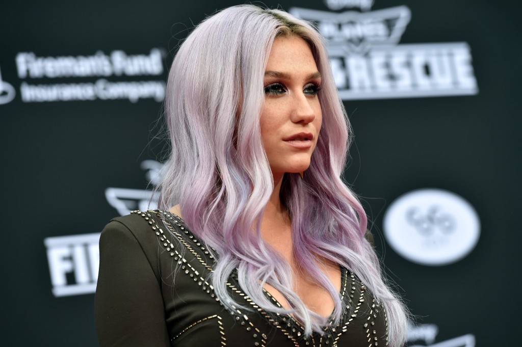 Kesha poses on the red carpet in a black dress and purple hair.