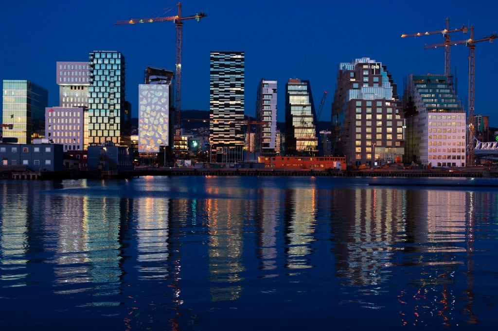 Buildings of The Barcode Project are reflected on the water at sunset in Oslo