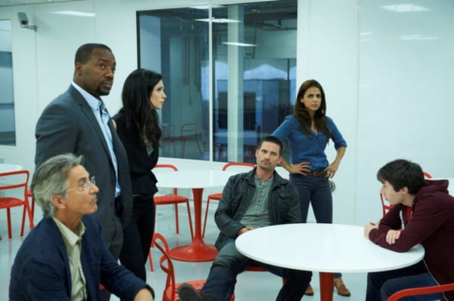 A group of men and women sit and stand around a table in Alphas