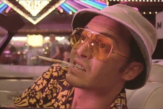 A man wearing sunglasses and smoking a cigarette leans over in his car. A man wearing sunglasses and smoking a cigarette leans over in his car.