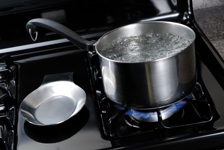 Pot of water boiling on a black natural gas stove.