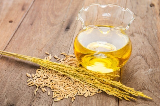 Rice bran oil in bottle glass and unmilled rice on wooden backgr