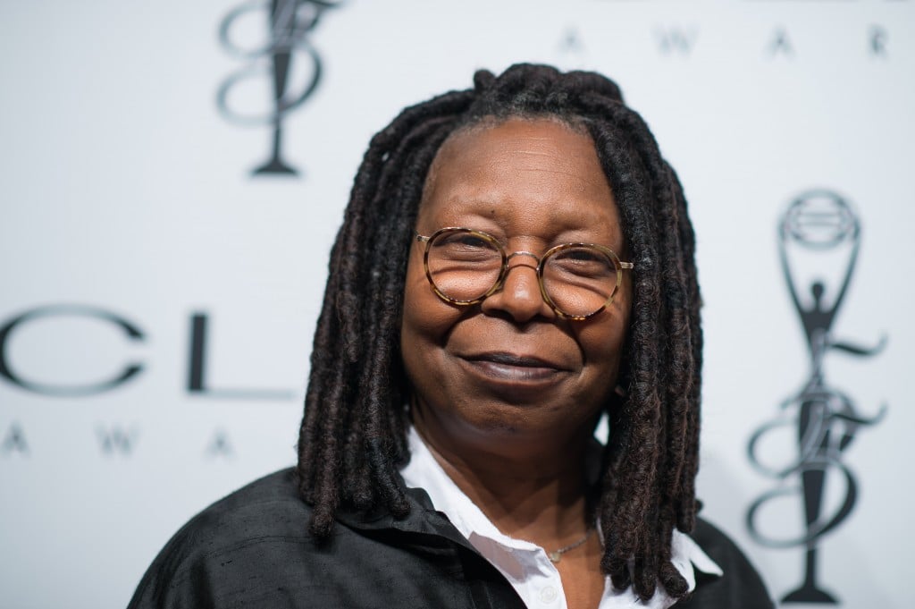 Whoopi Goldberg smiling while posing for photos on a red carpet.
