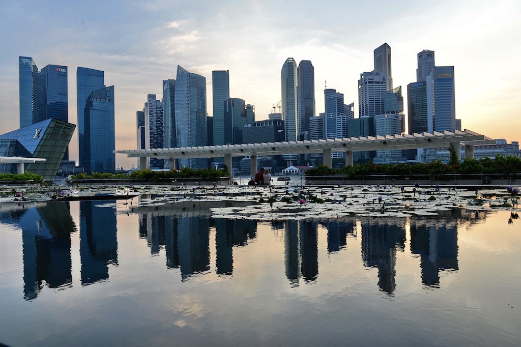 A general view of the financial district skyline is reflected in a pond in Singapore on March 6, 2014 in Singapore. Singapore played down a global survey showing that it is now the world's most expensive city, a finding which has triggered outrage among Singaporeans struggling with rising costs. Photo by Roslan Rahman/AFP/Getty Images.
