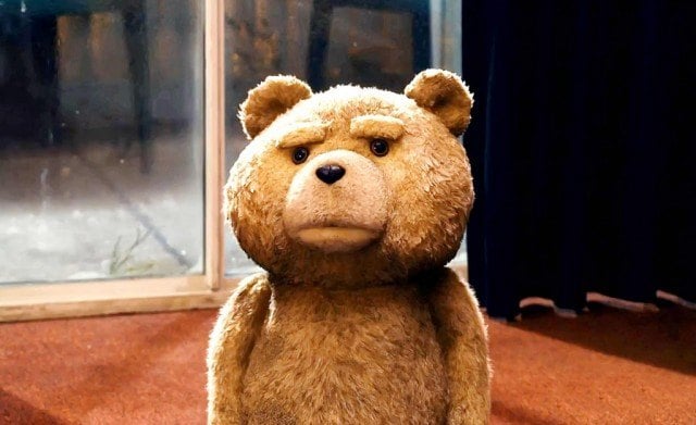 A grumpy-looking teddy bear stands in front of a door
