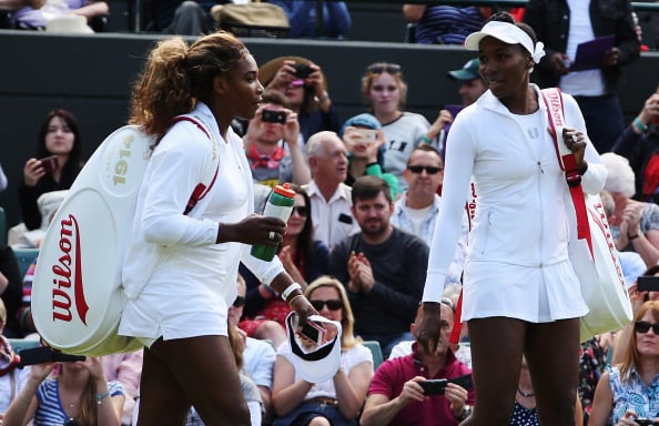 Serena and her sister stand in a tennis court in front of a crowd. Serena and her sister stand in a tennis court in front of a crowd.