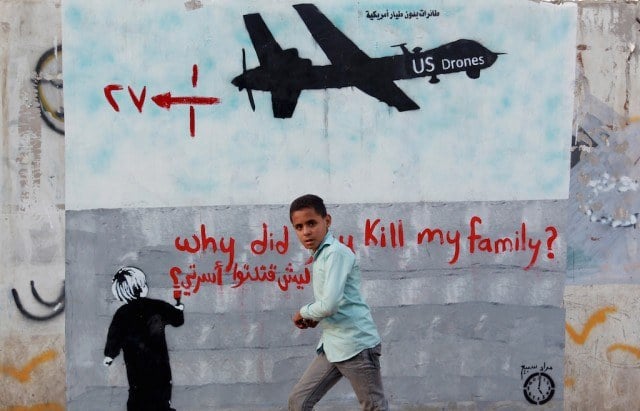 A Yemeni boy (C) walks past a mural depicting a US drone and reading ' Why did you kill my family' on December 13, 2013 in the capital Sanaa. A drone strike on a wedding convoy in Yemen killed 17 people, mostly civilians, medical and security sources said, adding grist to mounting criticism of the US drone war. (Photo by Mohammed Huwais/AFP/Getty Images)