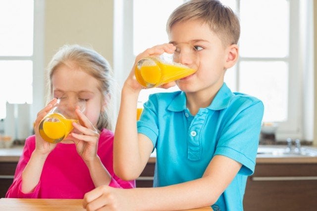 Siblings drinking orange juice in kitchen at home