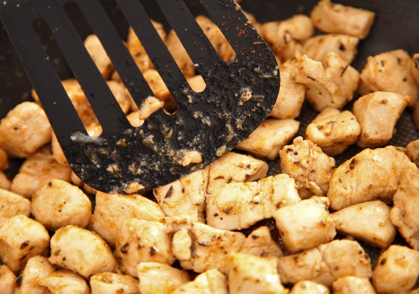 A nylon spatula pushes chicken in a pan