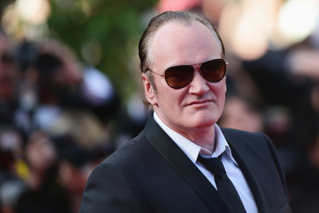 Quentin Tarantino wearing dark glasses and a suit and tie at a premiere. 