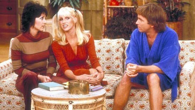 Joyce DeWitt, Suzanne Sommers, and Jhon Ritter sit together on a patterned couchinThree's Company