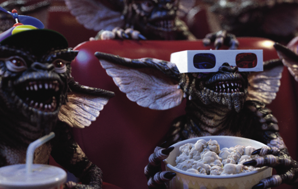 Gremlins watching a movie and eating popcorn and soda. 