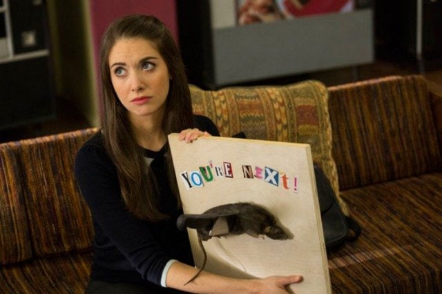 Alison Bris is sitting on a couch and holding up a poster.