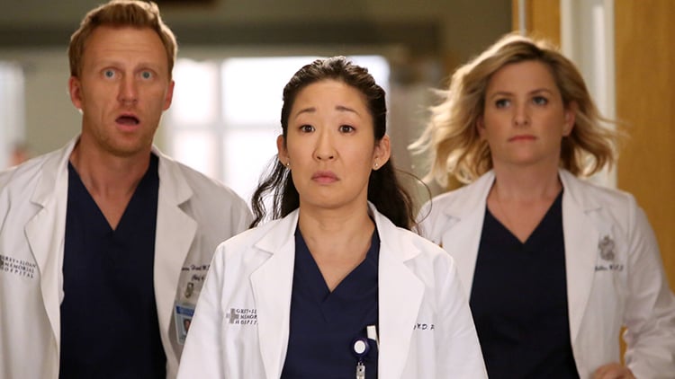 Three doctors from Grey's Anatomy look on in shock as they walk down a hallway