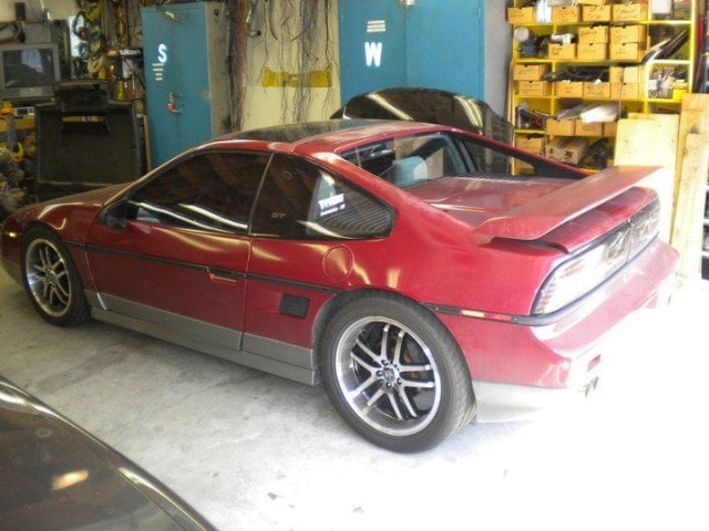 A red Pontiac Fiero sits parked inside a garage