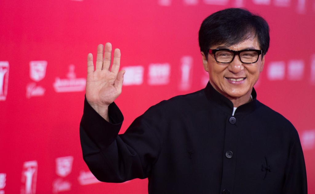 Jackie Chan holds up his hand in a wave while walking the red carpet