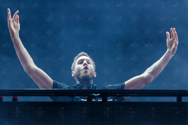 Calvin Harris has his arms up behind the DJ booth.