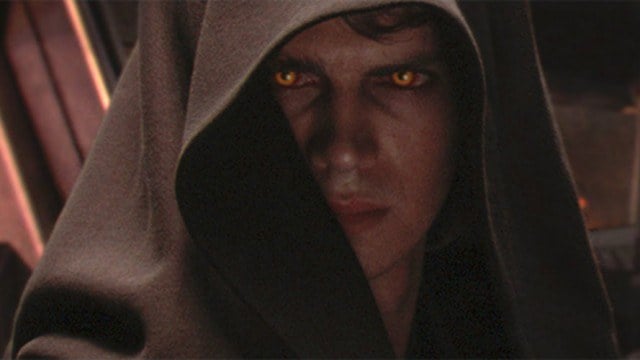Hayden Christensen as Anakin Skywalker with glowing yellow eyes looking serious under a brown hooded cloak in Star Wars: Episode III -- Revenge of the Sith