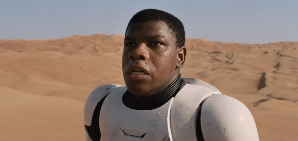 John Boyega stands in a desert while sweating and panting. 