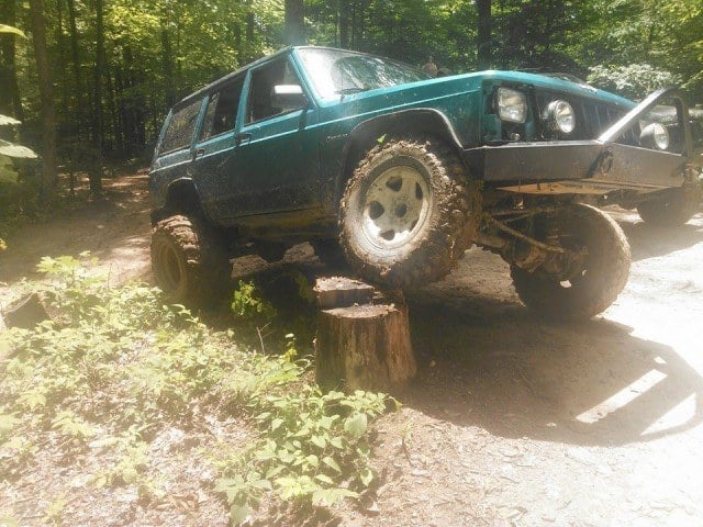 An aqua-colored Jeep Cherokee drives down some trails in the forest