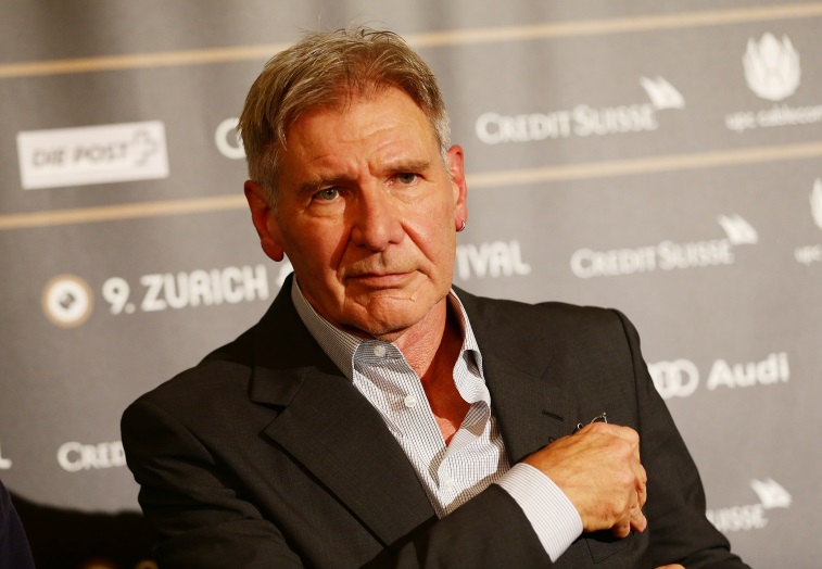 Harrison Ford is wearing an unbottoned shirt and a suit jacket.