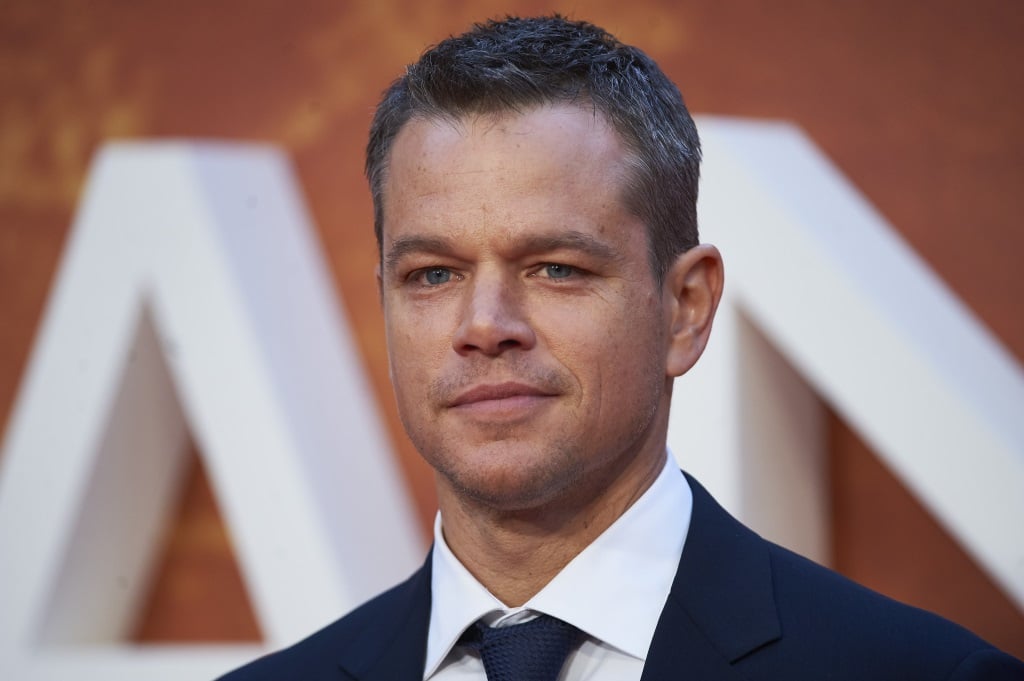 Matt Damon looks ahead and stands in a blue suit at an event
