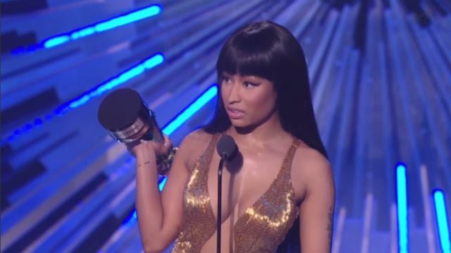 Nicki Minaj looks disgusted as she's on stage and holding her award.