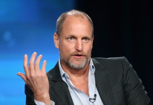 Woody Harrelson holds up his hand while speaking at a panel