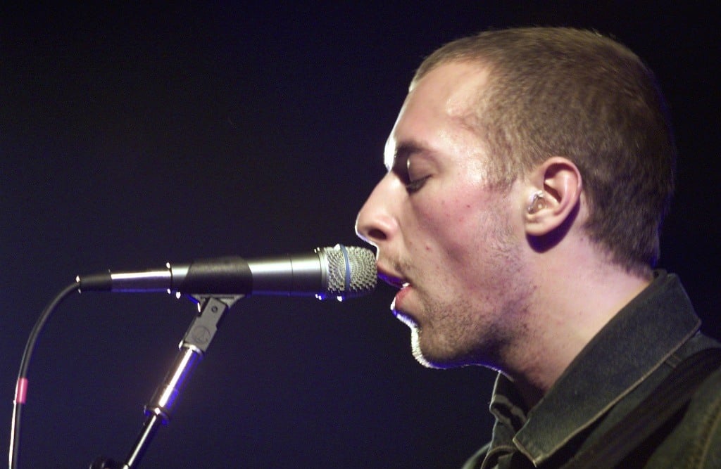 Coldplay lead singer Chris Martin is singing closely to a microphone.
