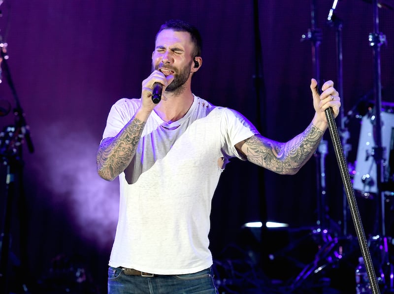 Adam Levine sings on stage in a white t-shirt.