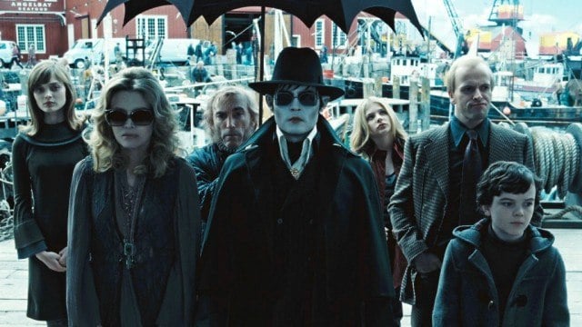 Johnny Depp and others in Dark Shadows standing under a black umbrella in a shipyard