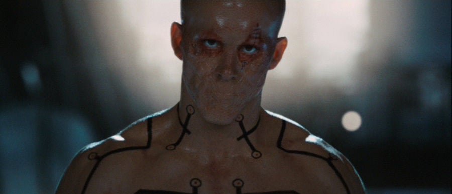 Deadpool, with his mouth sewn shut, shirtless and staring into the camera angrily