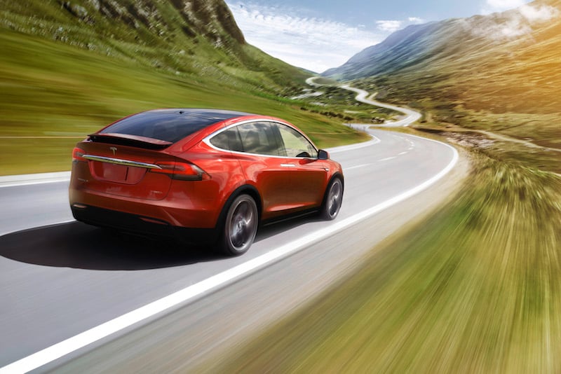 A red Tesla Model X speeding down a scenic road