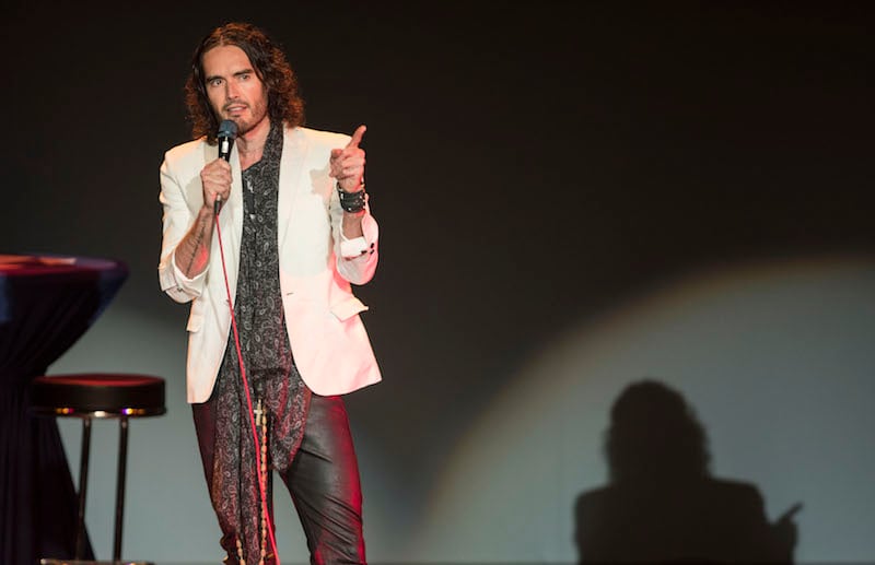 Russell Brand is talking on stage and holding a microphone.